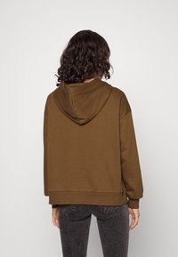 Felpa con cappuccio marrone a vestibilità rilassata, con polsini e orlo a coste. Texture morbida con un design minimalista. Senza loghi o motivi visibili.