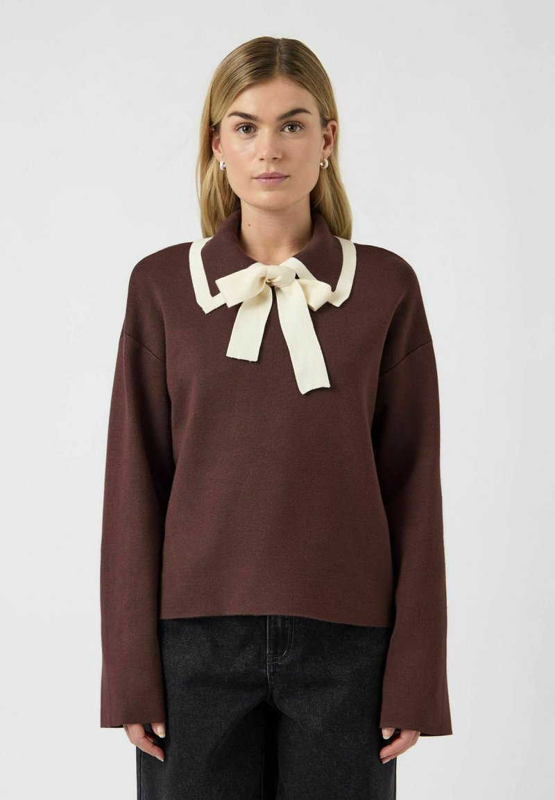 Brun genser med lange ermer, kremfarget krage og sløyfedetalj. Har en avslappet passform og myk tekstur. Bært med mørke jeans.