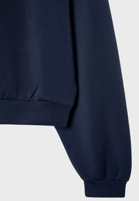 Manche et côté d'un sweat-shirt bleu marine montrant un bord-côte aux poignets et à l'ourlet, sur un fond gris clair uni.