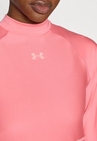 Αθλητική μπλούζα σε φωτεινό ροζ με ψηλό λαιμό, κατασκευασμένη από απαλό ύφασμα. Διαθέτει διακριτικό λογότυπο στο στήθος και λεπτομερείς ραφές κατά μήκος των ραφών.