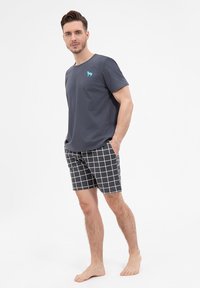 Szara koszulka z krótkim rękawem i niebieskim logo psa, zestawiona z czarnymi szortami w białą siatkę.