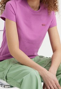 Lila bomull t-shirt med korta ärmar och rund halsringning, prydd med en liten röd Levi's-logotyp på bröstet, tillsammans med gröna cargobyxor.