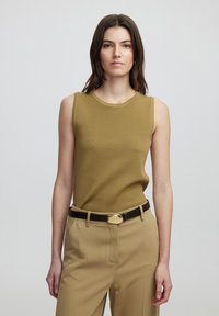 Top de punto sin mangas de color verde oliva con cuello redondo, combinado con pantalones beige de cintura alta y un cinturón negro con un broche dorado.