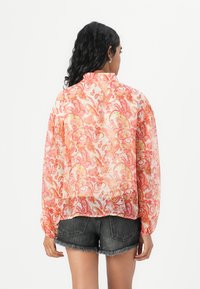 Sheer button-up shirt in pink and orange floral pattern, with long sleeves and elastic cuffs, paired with denim shorts.