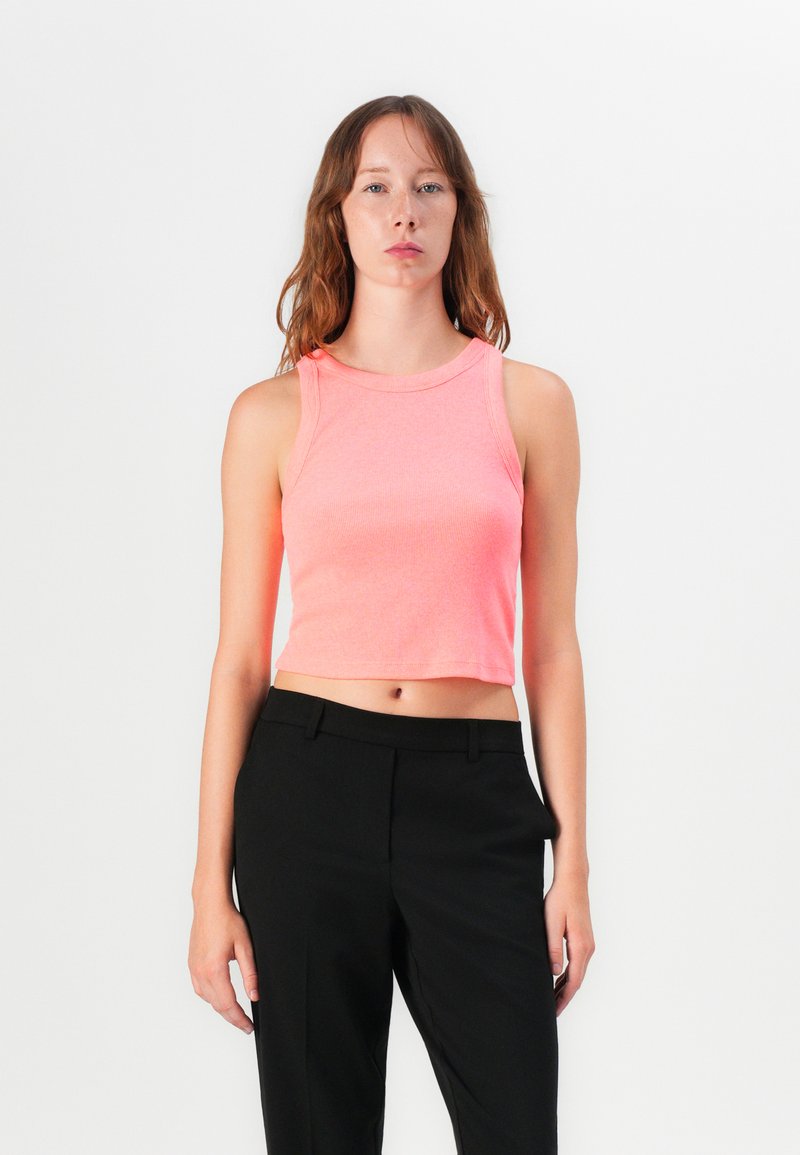 Bright pink cropped tank top with a ribbed texture and rounded neckline, paired with black tailored trousers.