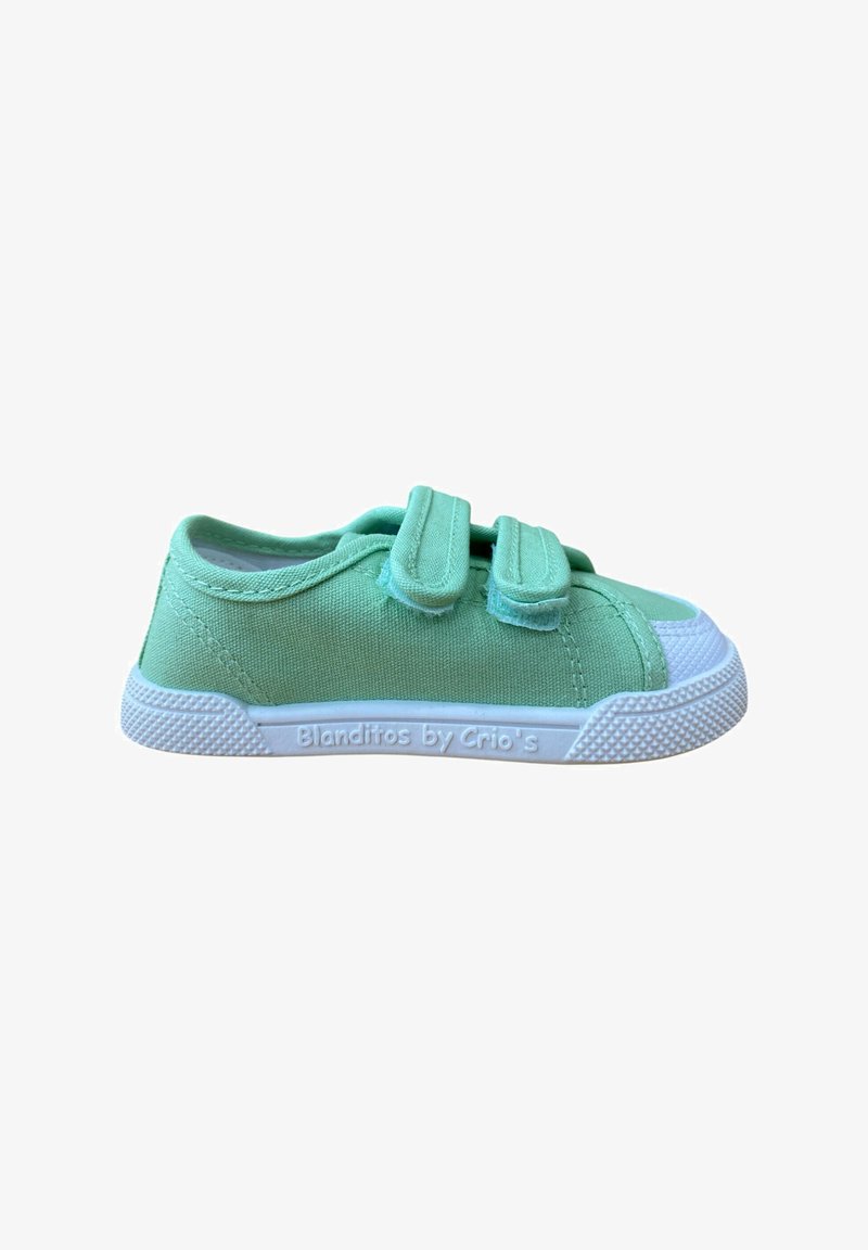 Zapatilla de lona verde con dos tiras de Velcro, puntera de goma blanca y suela texturizada. Marca visible en el lateral, diseño minimalista.