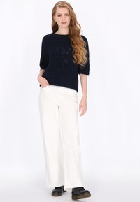 Granatowy sweter dzianinowy z krótkimi rękawami i teksturowanym wzorem, w połączeniu z białymi spodniami o szerokich nogawkach i czarnymi butami na sznurówki.