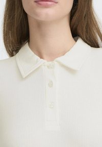 Ribbed, vaalean kremmivärinen polo-paita, jossa on klassinen kaulus, kolmonen napitus ja pehmeä rakenne, täydellinen rentoon käyttöön.