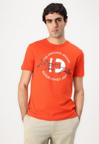 Orange bomulds T-shirt med rund halsudskæring, korte ærmer og et grafisk print med tekst og et logo i marineblå.