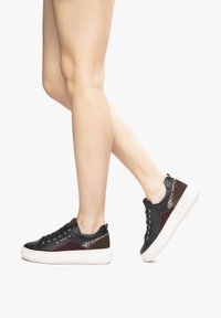 Sneaker nera e bordeaux con un design testurizzato, caratterizzata da accenti metallici e una suola in gomma bianca, mostrata in profilo laterale con i lacci.