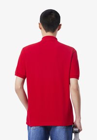 Röd polo skjorta med korta ärmar och krage, tillverkad av bomullsblandat tyg. Slät textur, avslutad med rak fåll.