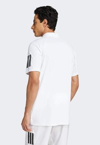 Hvit polo skjorte med svarte tre-stripes aksenter på ermene. Laget av glatt stoff, med klassisk krage og avslappet passform.