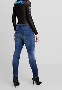 Džíny z modrého denimového materiálu s vysokým pasem a zaoseným vzhledem, středně vysoký pas, s zadními kapsami a oprýskanými detaily. V kombinaci s černými lodičkami na vysokém podpatku.