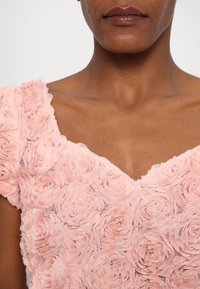 Gros plan sur une personne portant une robe rose à fleurs texturée avec un décolleté en V, montrant le cou, la clavicule et les lèvres.