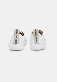 Baskets blanches basses avec un design en maille, des accents en cuir lisse, et un onglet de talon beige contrastant comportant du texte. Semelle en caoutchouc.