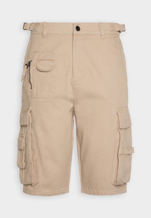 Beige cargobukser med flere lommer med klap og lynlås, bæltestropper og justerbare sidelommer ved taljen.
