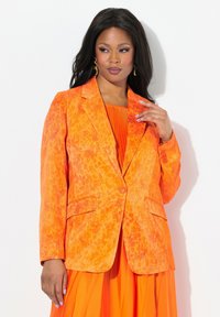 Blazer en un vibrante color naranja con un patrón texturizado de manchas de leopardo. Presenta un solo botón, solapas con muesca y dos bolsillos frontales.
