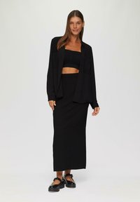 Schwarzes stricktop im Crop-Style kombiniert mit einem langen schwarzen Rock und einer lässigen Übergröße-Hemdjacke. Das Outfit zeichnet sich durch einen lockeren Schnitt und eine elegante Textur aus.
