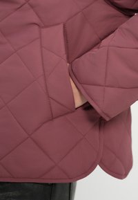 Κουκουλωμένο μπουφάν σε μαρουν απόχρωση με ομαλή υφή, που διαθέτει διαγώνιες ραφές, πλαϊνή τσέπη και στρογγυλεμένο τελείωμα.