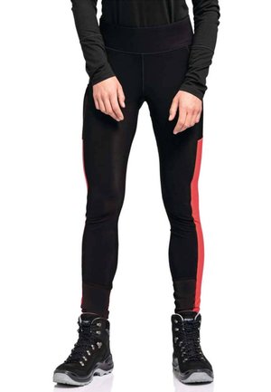 Leggings noirs avec des bandes latérales rouges, taille moyenne, tissu extensible, associés à des bottes de randonnée noires avec des œillets en argent et des semelles grises.