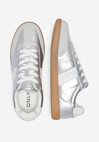 Baskets synthétiques argentées avec des accents blancs, tige texturée, lacets blancs et semelle en caoutchouc gomme. Logo latéral visible. Design athlétique classique.