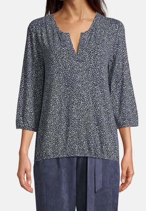 Femme portant un haut à manches longues bleu et blanc à motifs avec un décolleté fendu et un pantalon ample bleu foncé.