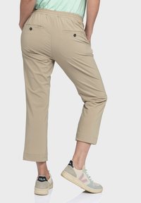 Beige Cropped-Hosen mit elastischem Bund, ausgestattet mit zwei Gesäßtaschen mit schwarzen Knöpfen und einem glatten, leichten Stoff.