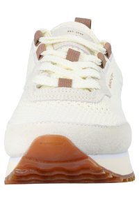 White sneakers featuring a knitted upper, suede accents, and beige laces. The sole is cream with a textured brown rubber base.