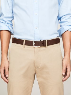 Brown leather belt with silver hardware, worn over light beige pants and a light blue shirt, showcasing a clean, classic design.