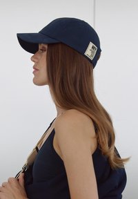 Casquette de baseball bleu marine en tissu, avec une visière courbe et une étiquette rectangulaire à l'arrière portant du texte et un code-barres.