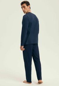 Navy niebieski, podłużnie paskowany top z długim rękawem i okrągłym dekoltem, w połączeniu z jednolitymi, granatowymi spodniami, prezentującymi luźny krój i miękką teksturę.