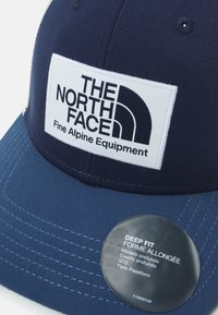 Kék baseball sapka fehér logóval, amelyen a "The North Face" és a "Fine Alpine Equipment" felirat található. Mélyen illeszkedő kialakítás, strukturált anyaggal.