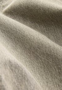 Gros plan d'un tissu tissé marron clair avec des plis doux et des détails de texture visibles.