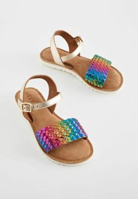 Flerfärgade flätade sandaler med ett metalliskt guldrem, en brun mocka fotbädd och en vit gummisula. Utformade för komfort och stil.