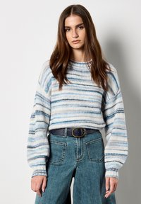 Sweter w paski w odcieniach niebieskiego, białego i szarego, z okrągłym dekoltem i balonowymi rękawami, zestawiony z spodniami dżinsowymi z wysokim stanem i ciemnym paskiem.