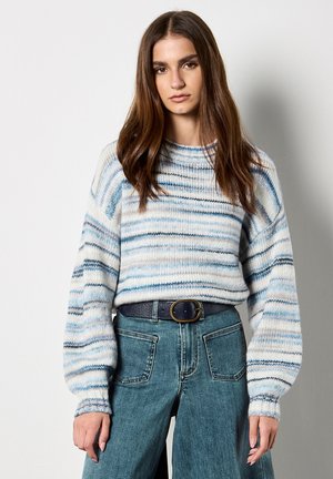 Maglione a righe nei toni blu, bianco e grigio, con scollatura rotonda e maniche a palloncino, abbinato a pantaloni in denim a vita alta e una cintura scura.