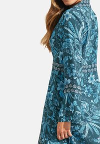 Blauwe jurk met bloemenprint, lange mouwen, een hoge kraag en een patroon op de tailleband. Heeft een zachte stoftextuur.