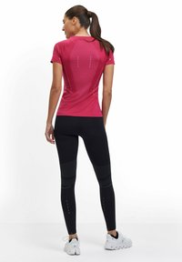 Korte mouwen, fuchsia sporttop met reflecterende accenten en zwarte, aansluitende legging met textuurpanelen en roze details. Witte sneakers.