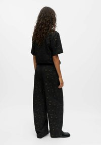 Schwarzes Zweiteiler-Outfit mit einem lockeren Kurzarmoberteil und weiten Beinen, verziert mit einem subtilen Blumenmuster in Dunkelgrün und Braun.