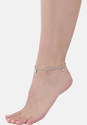 Bracelet alla caviglia in argento con un design a catena e tre charm: una conchiglia, una stella marina e una forma astratta. Texture liscia, stile minimalistico.