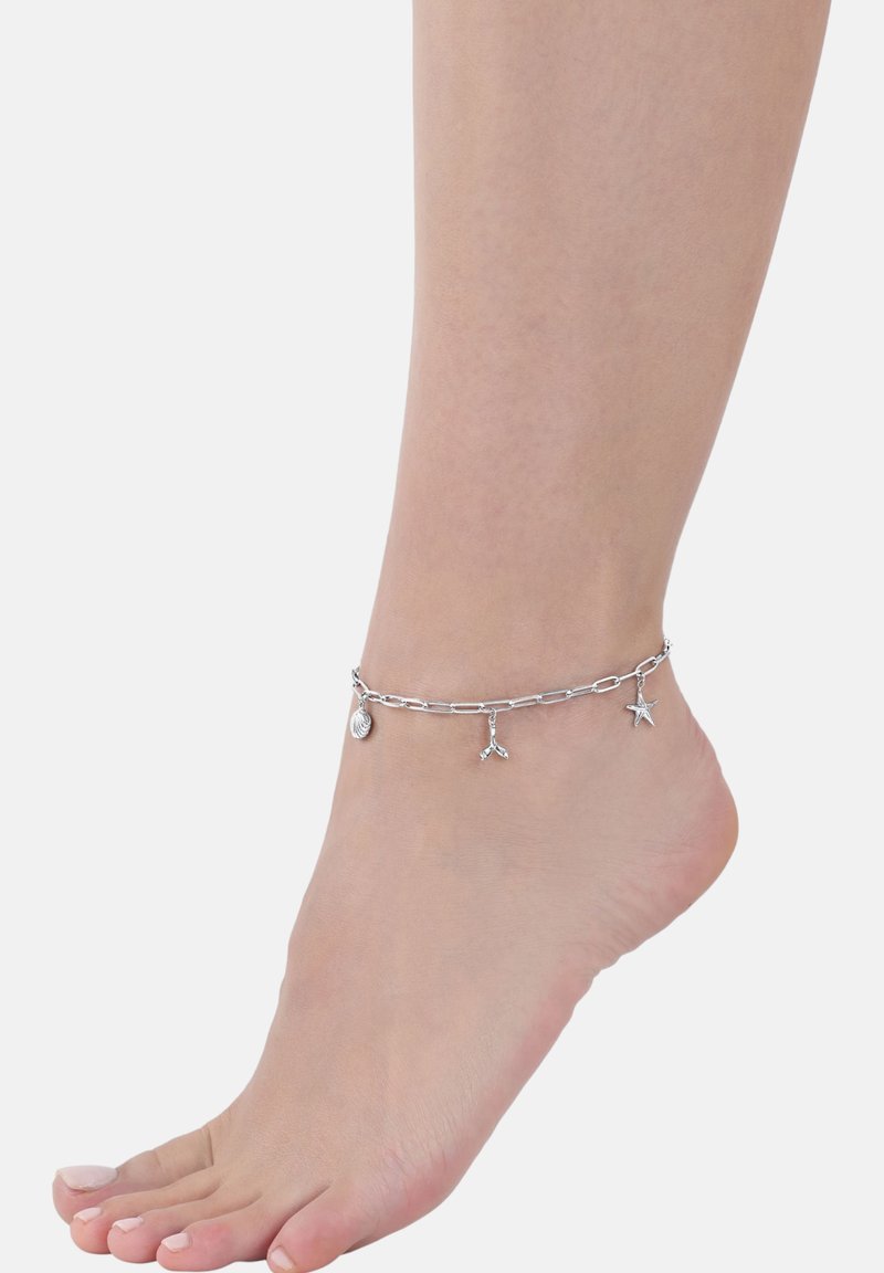 Bracelet alla caviglia in argento con un design a catena e tre charm: una conchiglia, una stella marina e una forma astratta. Texture liscia, stile minimalistico.