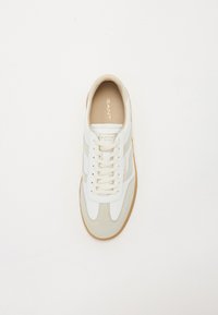 Tenisici din piele albă cu accente de suede bej, șireturi groase de culoare crem și o talpă din cauciuc de culoare maro deschis. Prezintă brandingul "GANT" pe limbă.