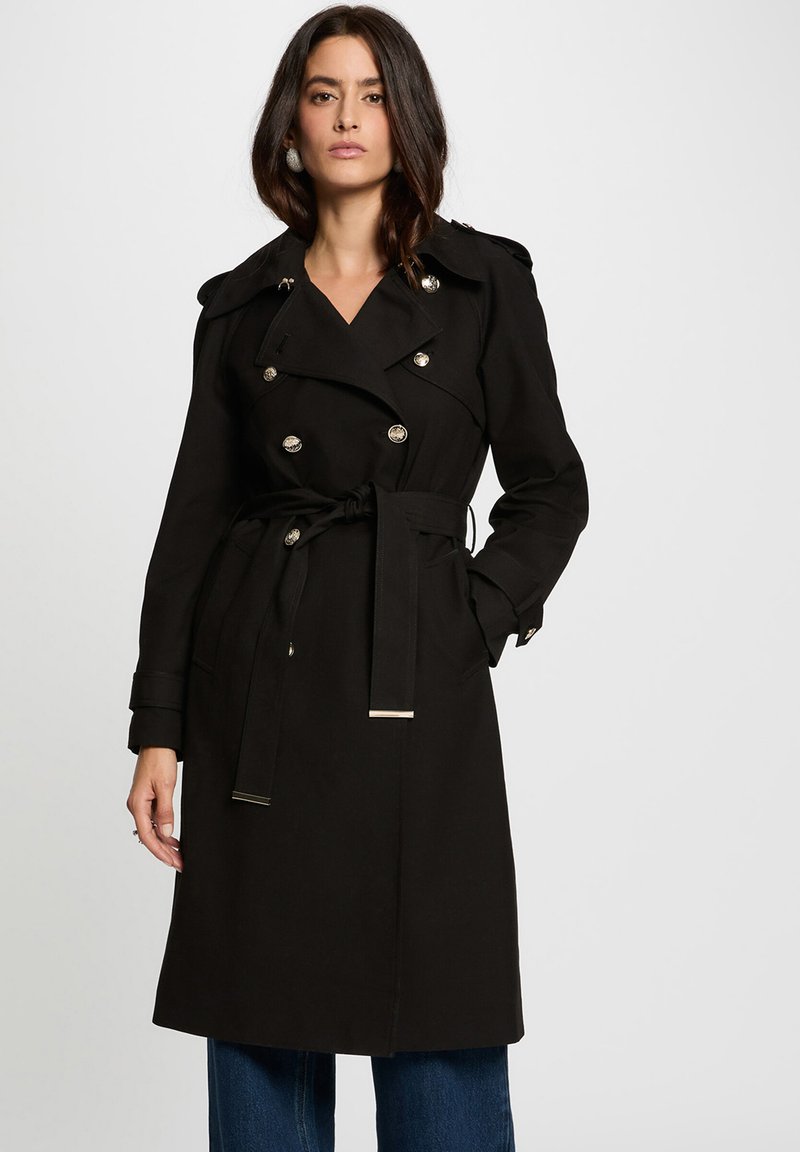 Cappotto lungo nero con design doppiopetto, bottoni argentati, ampi rever e vita con cintura. Presenta maniche lunghe e un taglio al ginocchio.