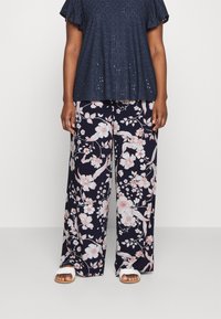 Maritiem bloemen top met oogjespatroon, gecombineerd met wijde broek met grote roze en witte bloemenpatronen. Witte sandalen maken de outfit compleet.