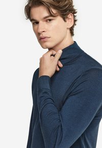 Marinblå polokrage tröja i mjukt stickat material, med lång ärm och en åtsittande design. Texturen är slät med en lätt lyster.