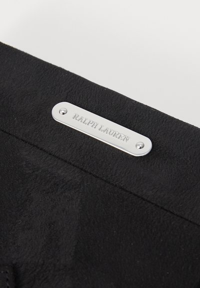 Svart semsket materiale med en teksturert overflate; har en sølvmetallplate gravert med "RALPH LAUREN." Enkelt og elegant designdetalj.
