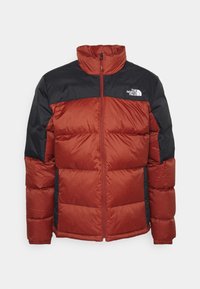 Přisoňová bunda s vínovým tělem a černými rameny, která má vysoký límec, přední zip a logo North Face na horní levé straně.