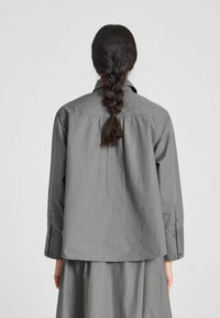 Camicia grigia a maniche lunghe con piega sul retro, polsini abbottonati e una vestibilità morbida, realizzata in tessuto leggero, progettata per un look informale.