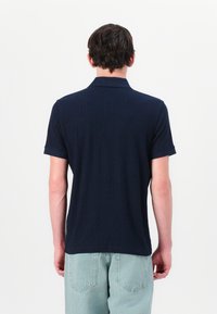 Polo shirt azul marinho com riscas, com colarinho, mangas curtas e um corte descontraído. O material parece macio, com uma textura subtil. Vista da parte de trás mostrada.