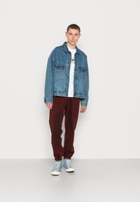 Jaqueta de ganga com dois bolsos no peito, cor azul clara, combinada com calças vermelho-escuras e sapatilhas altas azul claras. T-shirt branca simples por baixo.